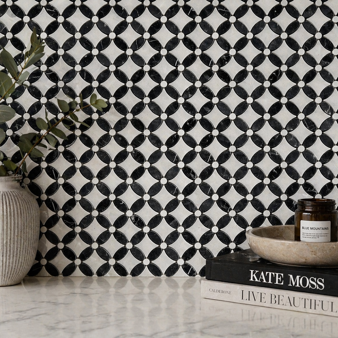 Black and white patterned wall tile with a vase, books, and candle on a surface.