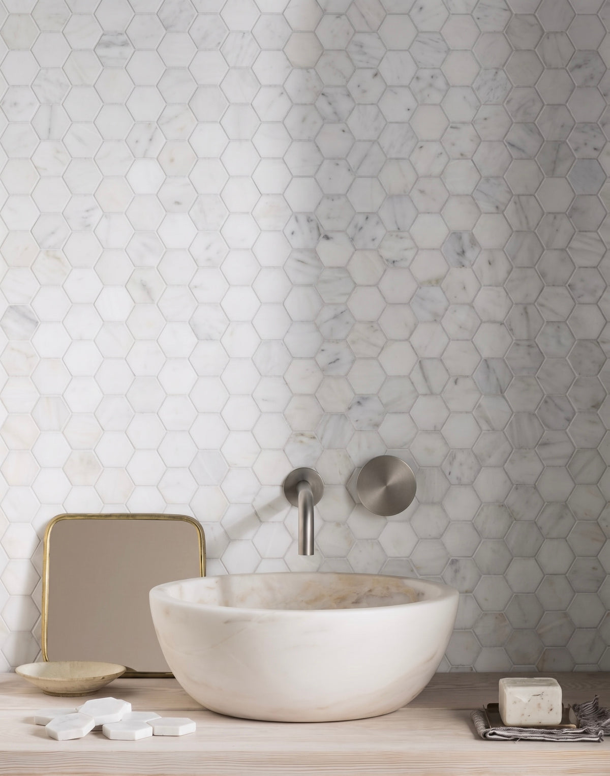 Carrara white honed marble hexagon mosaic on a bathroom wall behind a stone basin