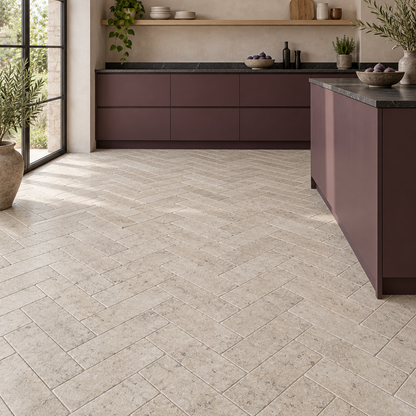 Dijon tumbled limestone 50 x 200 mm tiles laid in herringbone on a kitchen floor with plum cabinets.